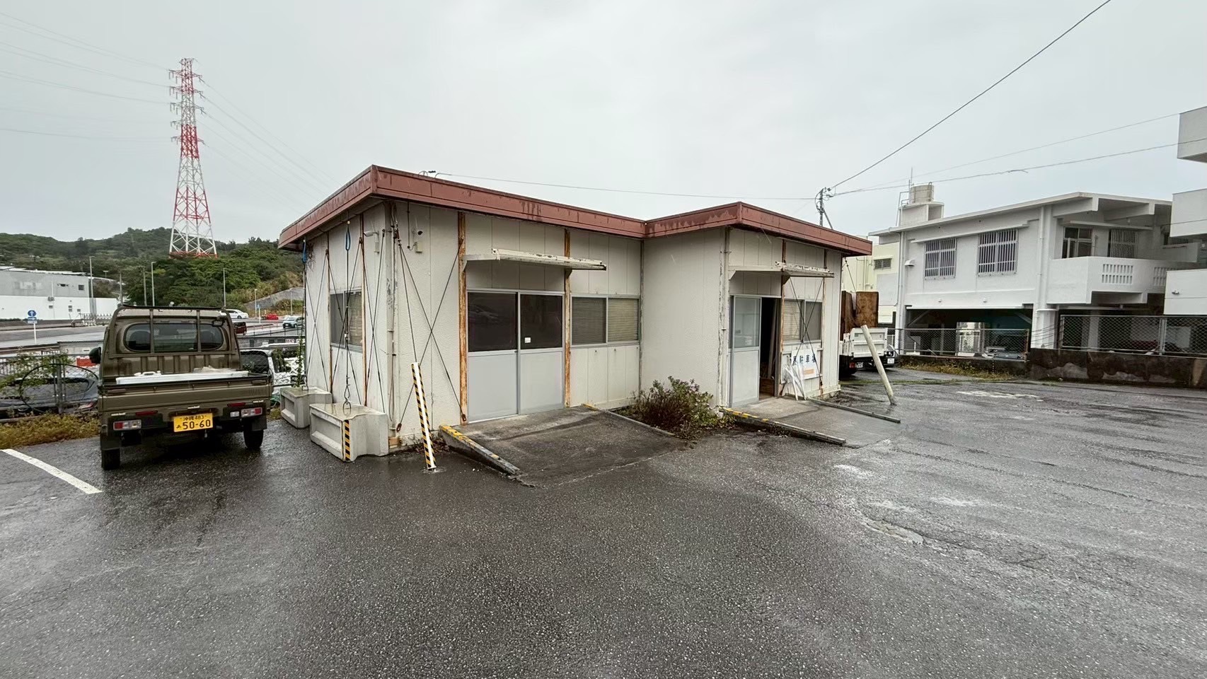 名護市の駐車場に建つL字型のプレハブ事務所